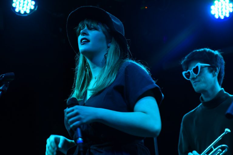 Sarah Gross performs at Funk n' Waffles while trumpeter Liam Hines, sporting heart-rimmed sunglasses, looks on.