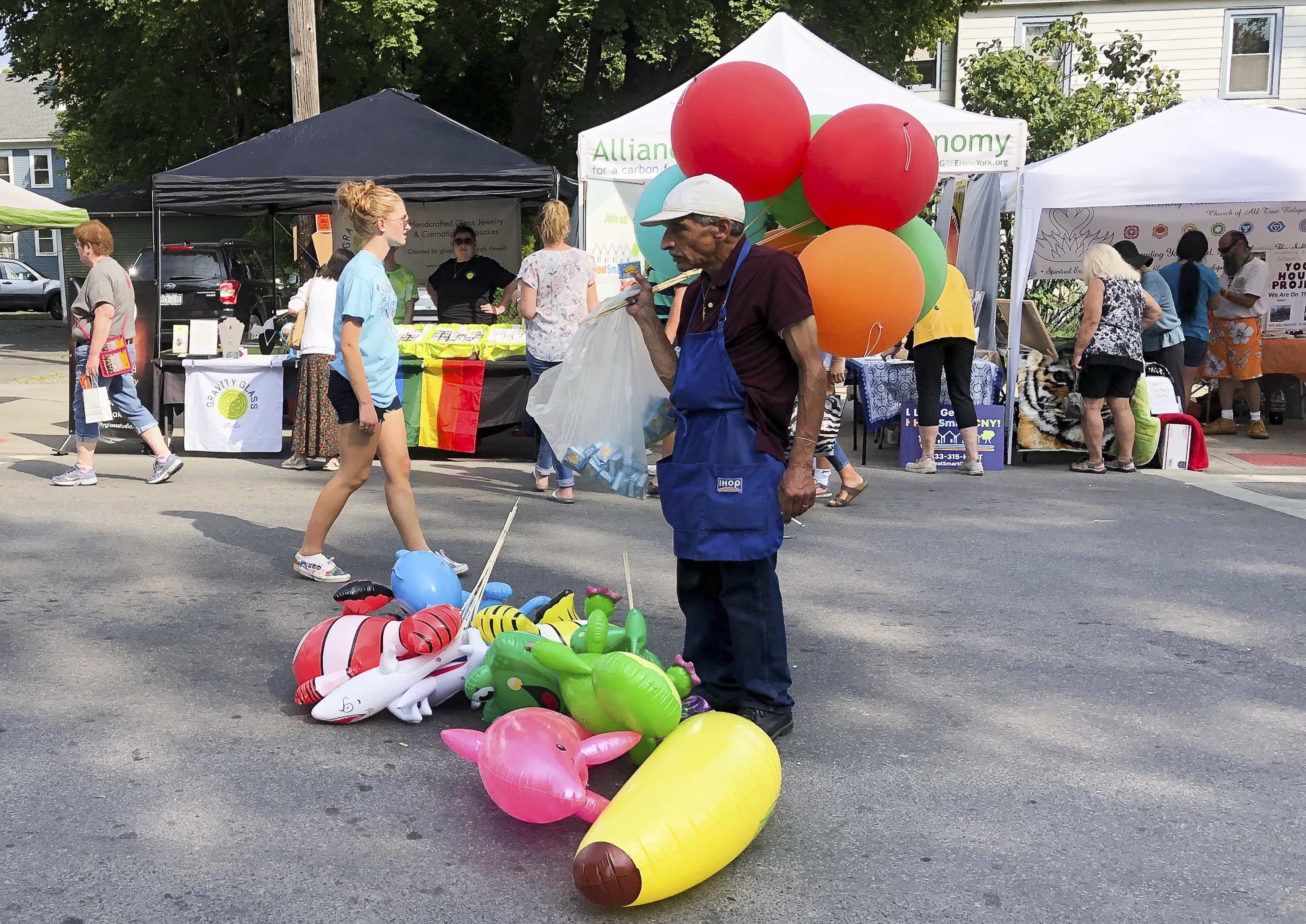 A baloon salesman stands in the street smoking.