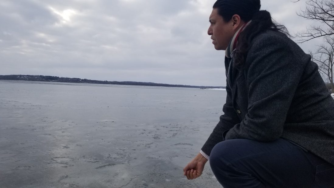 Powless kneels on the rocky shore of Onondaga Lake, cupping the water in his hand as he gives a silent prayer.