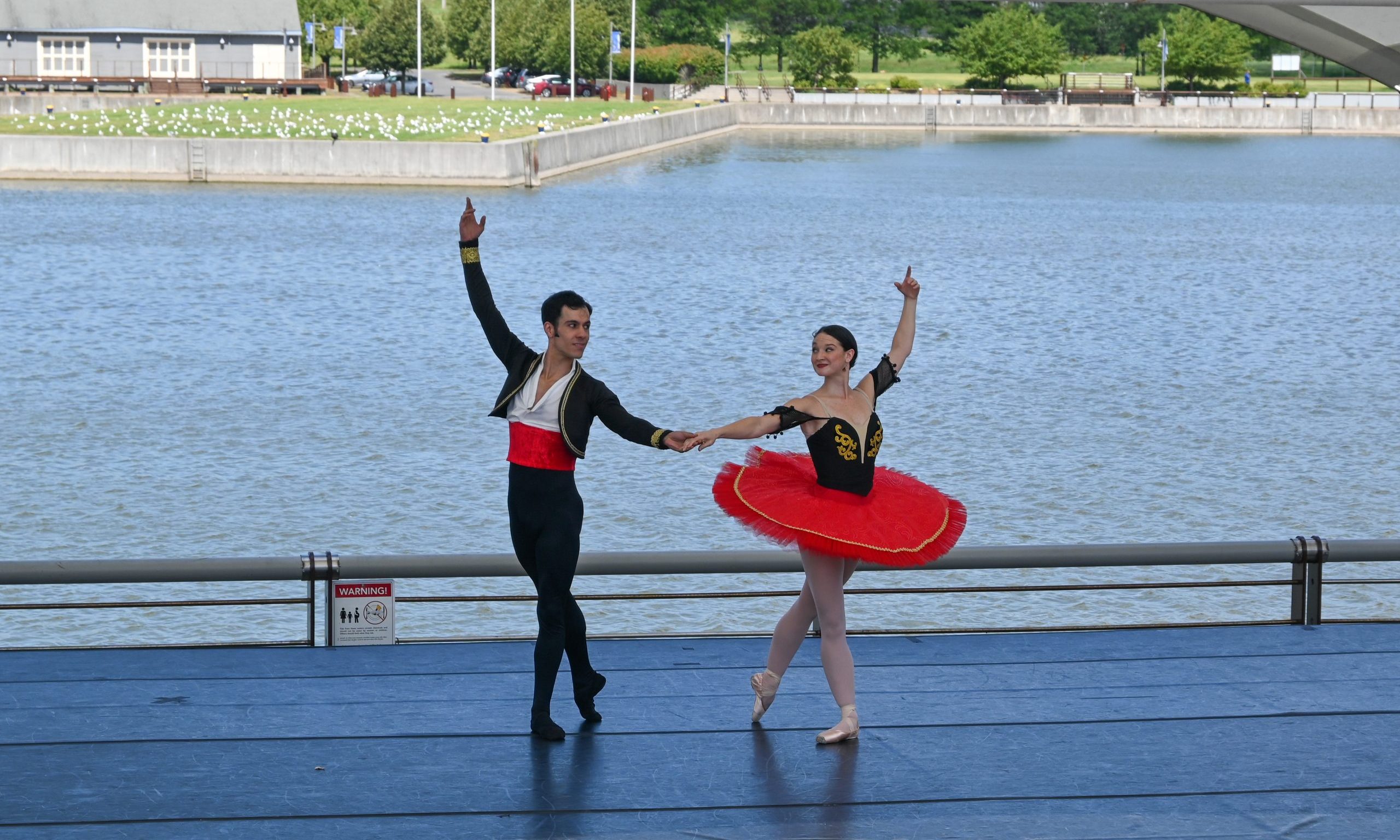 Two Ballerinas holding hands with one arm up in the air smiling at each other during their performance