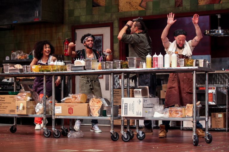 Four people onstage, acting in a kitchen scene