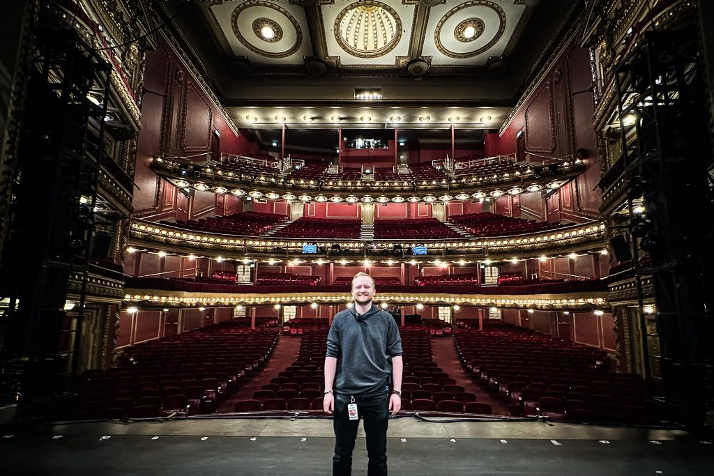 SU alumni Nate Coffey stands on stage on set as a production manager.