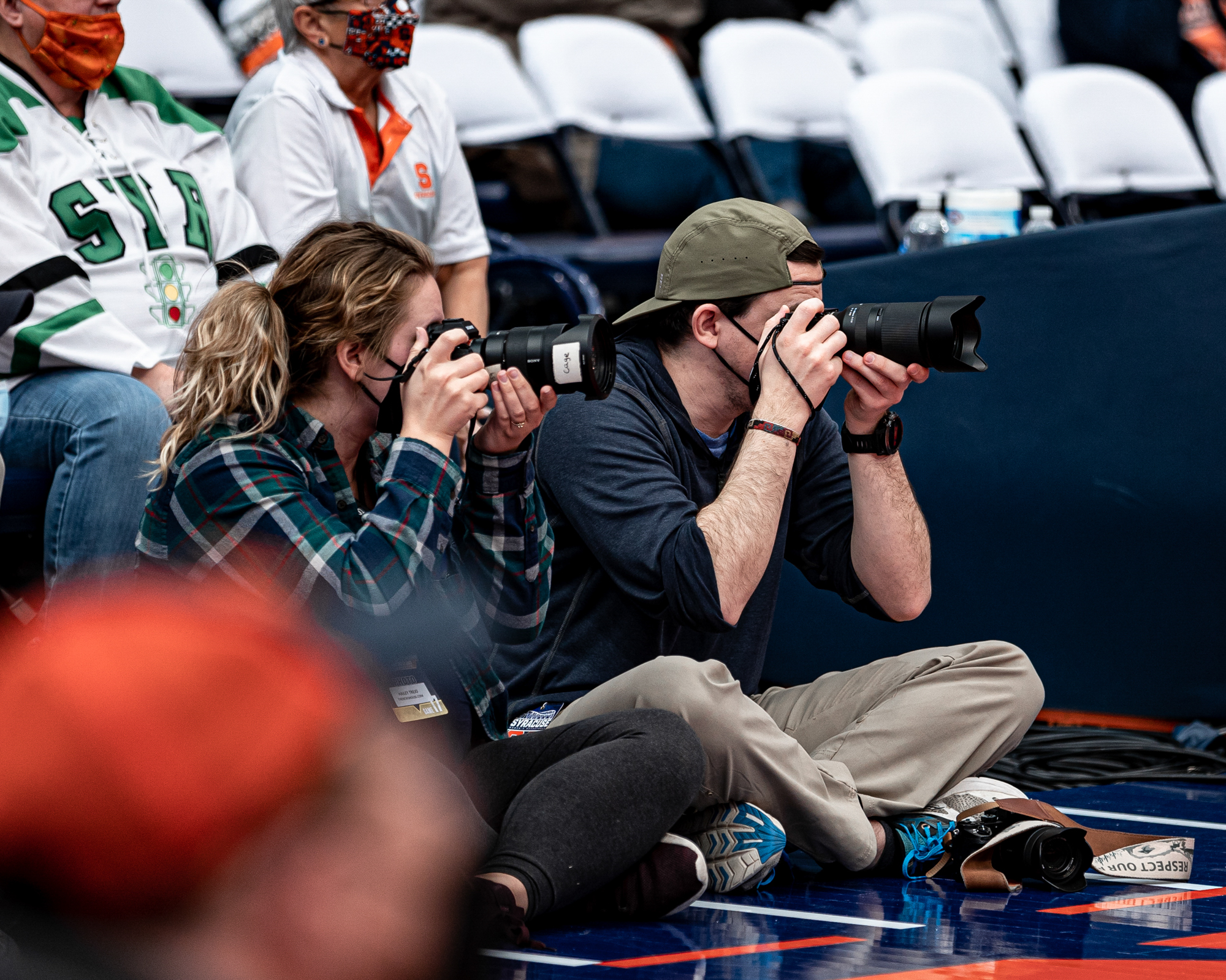 Hailey Trejo and Erik Makic take photos at a basketball game