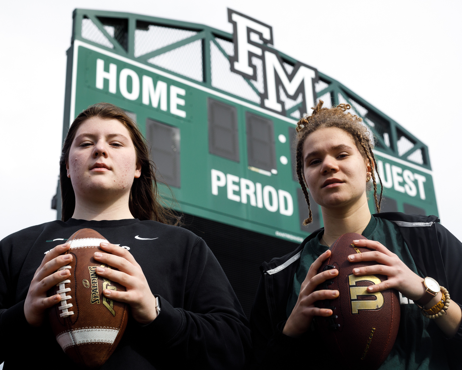 Mara McBride and Julia Leary hold footballs on the football field