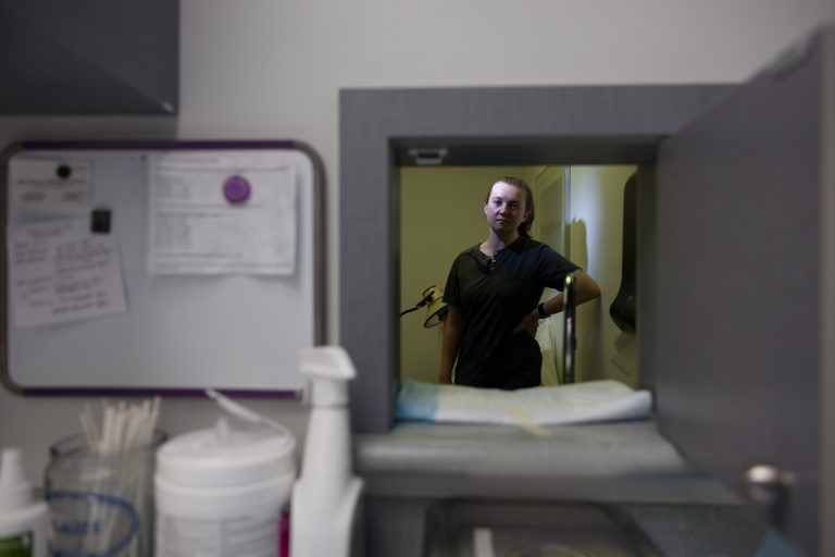 Ellen Armstrong poses for a photo through medical cubby in an exam room