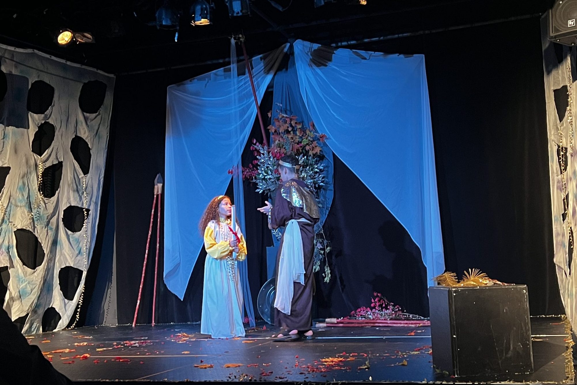 Emely Dominguez-Lambert and Michael Alberti stand on a decorate stage and act out a scene from a play
