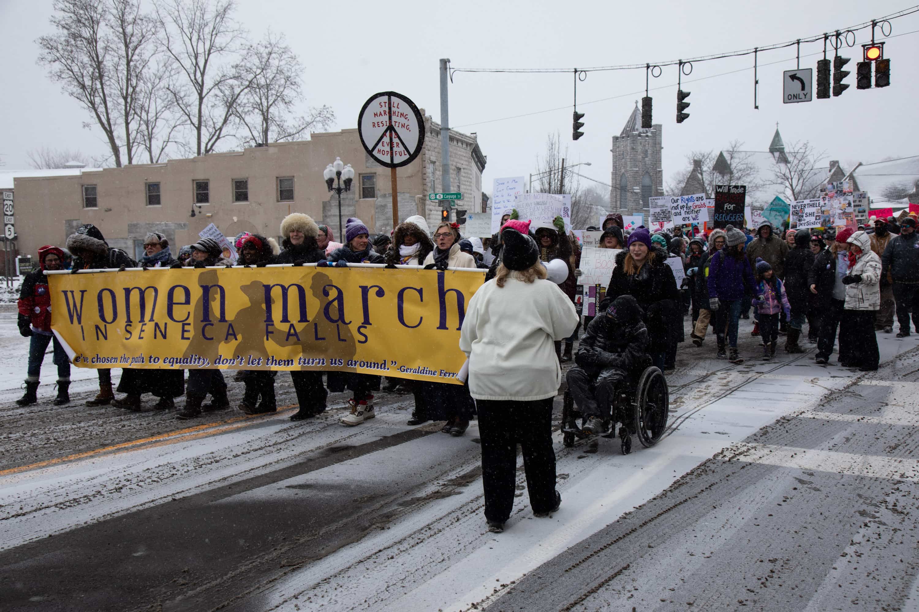 Activists including Leader of Ceremonies, Maureen Quigley; Colleen Kattau, Rev Leah Ntuala Pastor; Diana Smith, Mayor of Seneca Falls (former); Suffragist Descendents, Coline Jenkins and Elisa Kellogg Shaffer; Gwen Webber-McLeod, CEO, Gwen, Inc; Sally Roesch Wagner, author and Matilda Joslyn Gage Center, Executive Director lead the Women’s March from Trinity Park in Seneca Falls this morning, Saturday, January 19th.