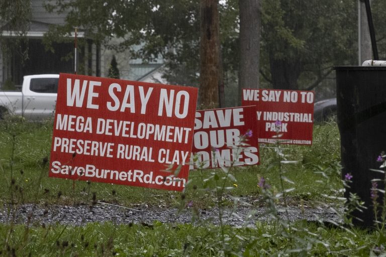 Bright red signs are displayed on the lawns of multiple homes on Burnet Road in Clay.