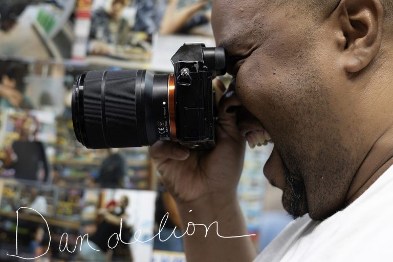 Man holds camera to his eye to photograph customer in a Syracuse, New York, convenience store.