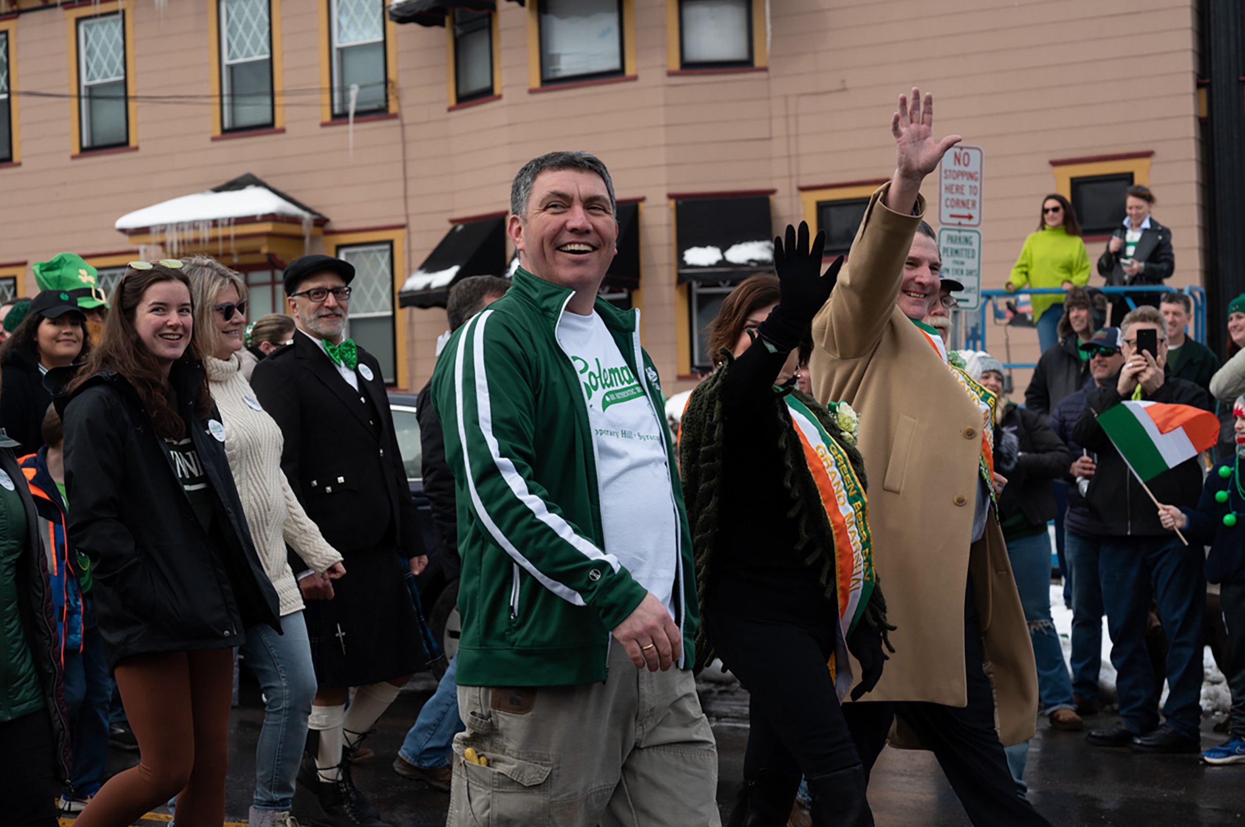 Dennis Coleman, son of Peter Coleman, walks with this year's Green Beer Day Grand Marshalls Mike and Mary Kay Ryan (pictured with their hands waving).