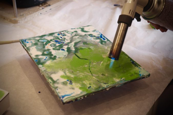 Sally Hootnick uses a blowtorch to heat up beeswax-based encaustic paints on a wooden board.