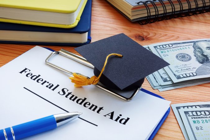 Federal student aid papers and small Square academic cap.