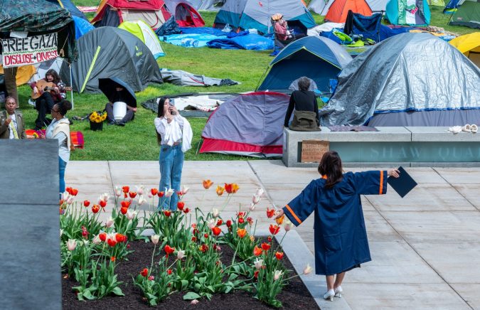 A soon-to-be Syracuse University graduate has a photo taken Thursday in front of Hendricks Chapel adjacent to the pro-Palestine encampment.
