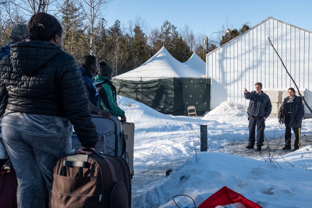 Canadian border patrol confront migrants from Cameroon and Uganda as they cross the border at Roxham Road with their luggage on March 1.