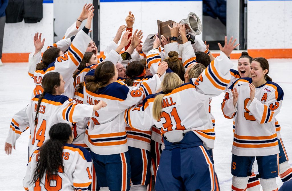 The Syracuse women's hockey team celebrates with the CHA trophy after scoring in overtime.