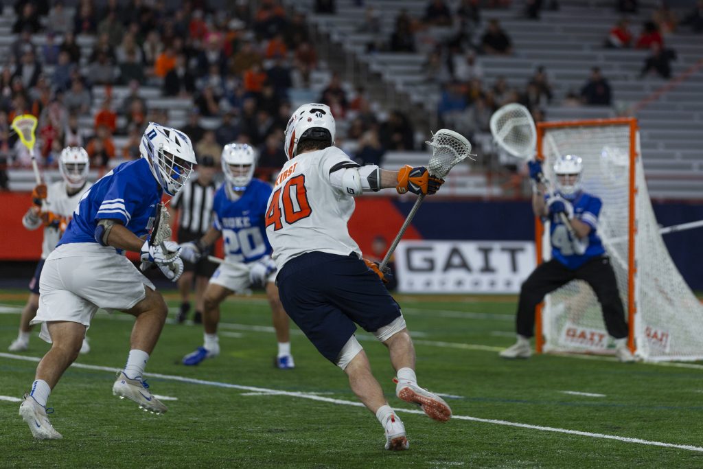 Syracuse's Cole Kirst drives to goal as a Duke defender checks him.