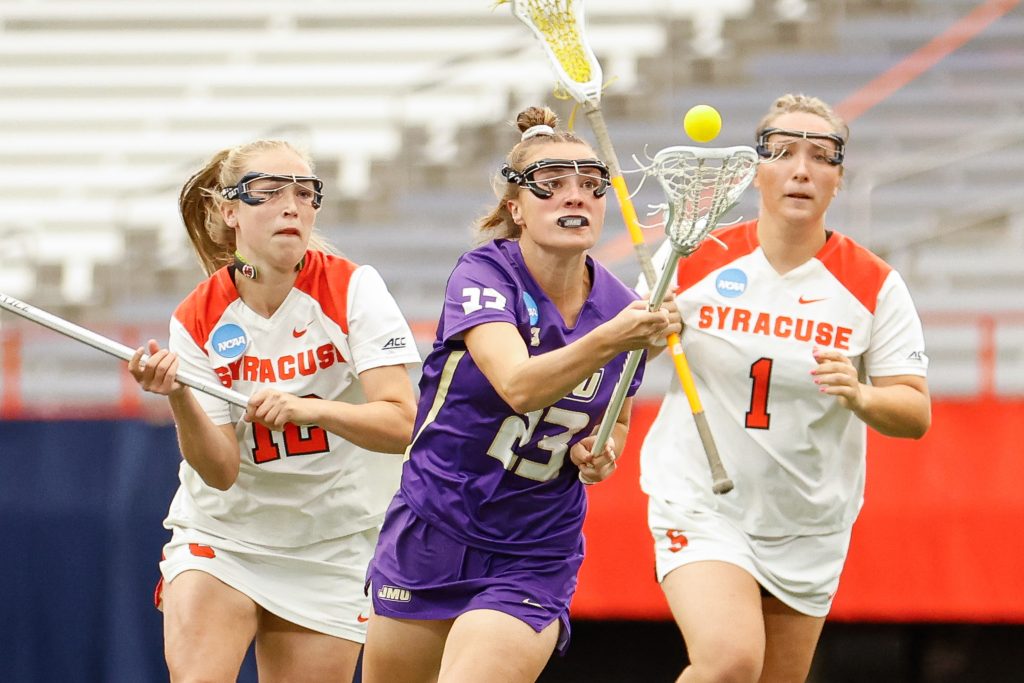 James Madison's Taylor Marchetti (23) eyes a catch as Syracuse's Katie Goodale (12) and Olivia Adamson (1) follow close behind during the NCAA Tournament quarterfinal on Thursday, May 18, 2023 at JMA Wireless Dome. Photo by Kayla Breen.