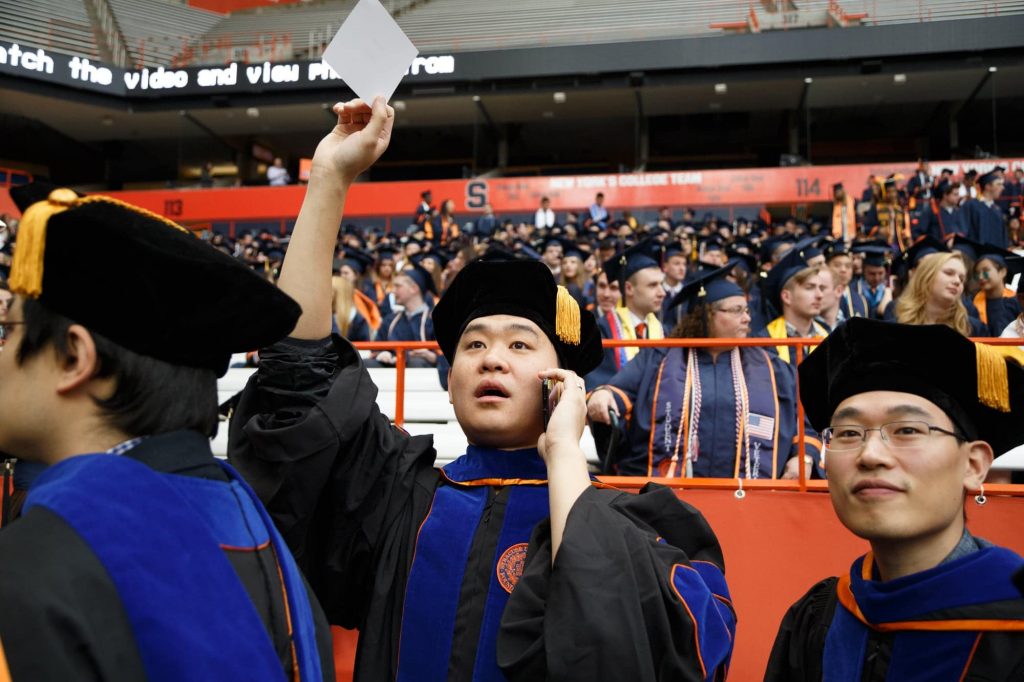 A doctoral candidate tries to find his loved ones in a sea of people seated all over the Carrier Dome.