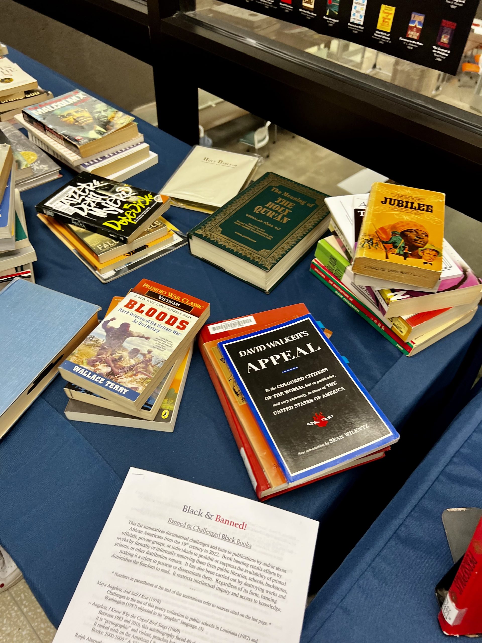 Various books are laid out and stacked near each other on a table with a blue tablecloth.